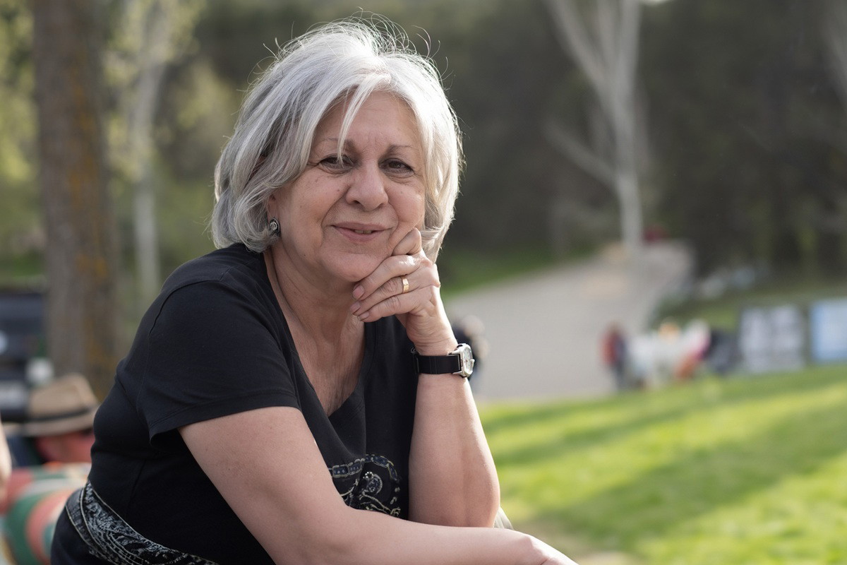 kobieta w wieku 65 lat siwe włosy stoi na ganku na tle wiosennego ogrodu zamyślona