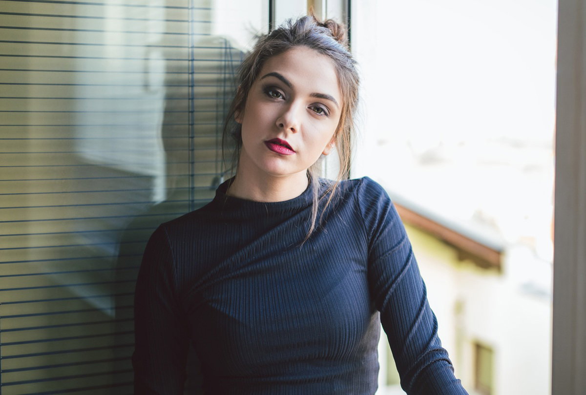 kobieta w wieku 25 plus w ciemnej bluzce stoi na tle balkonu zamyślona