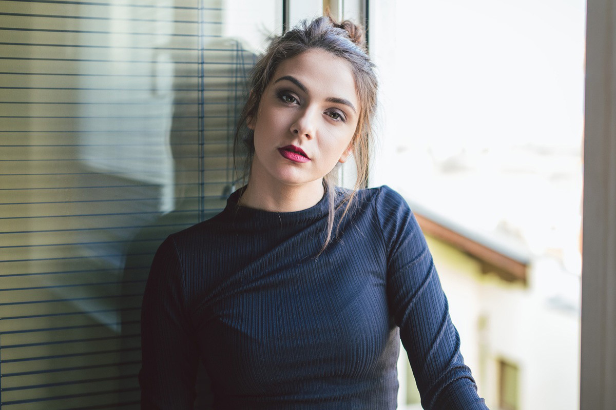 kobieta w wieku 25 plus w ciemnej bluzce stoi na tle balkonu zamyślona