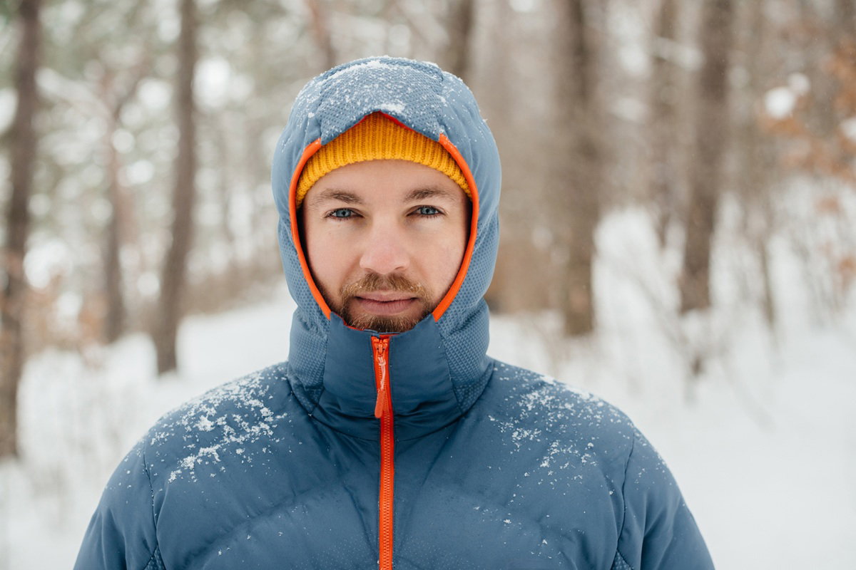 mężczyzna w wieku 30 plus w jasnoniebieskiej kurtce z pomarańczowymi akcentami i w kapturze stoi z poważna miną