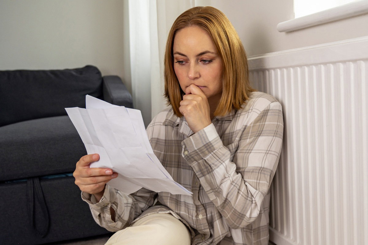 kobieta w wieku 40 plus w koszuli w kratę siedzi na ziemi i czyta kartki zamyślona i poruszona