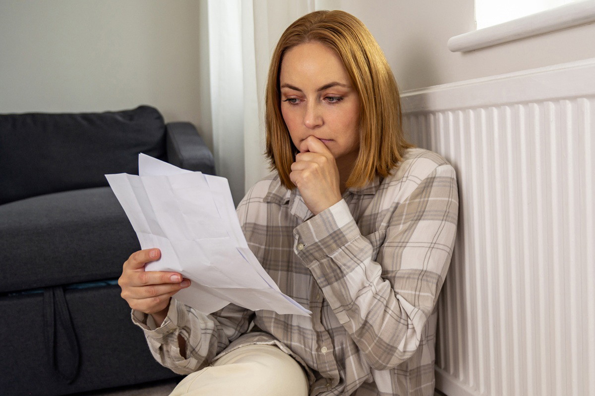 kobieta w wieku 40 plus w koszuli w kratę siedzi na ziemi i czyta kartki zamyślona i poruszona