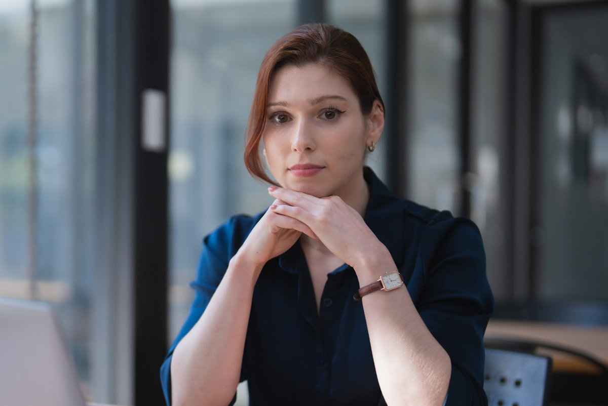 kobieta w wieku 30 plus z upiętymi włosami siedzi przy biurku w biurze z poważną miną