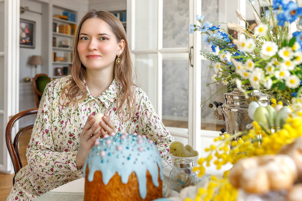 kobieta w wieku 30 plus siedzi przy wielkanocnym stole z babą drożdżową i lekko się uśmiecha