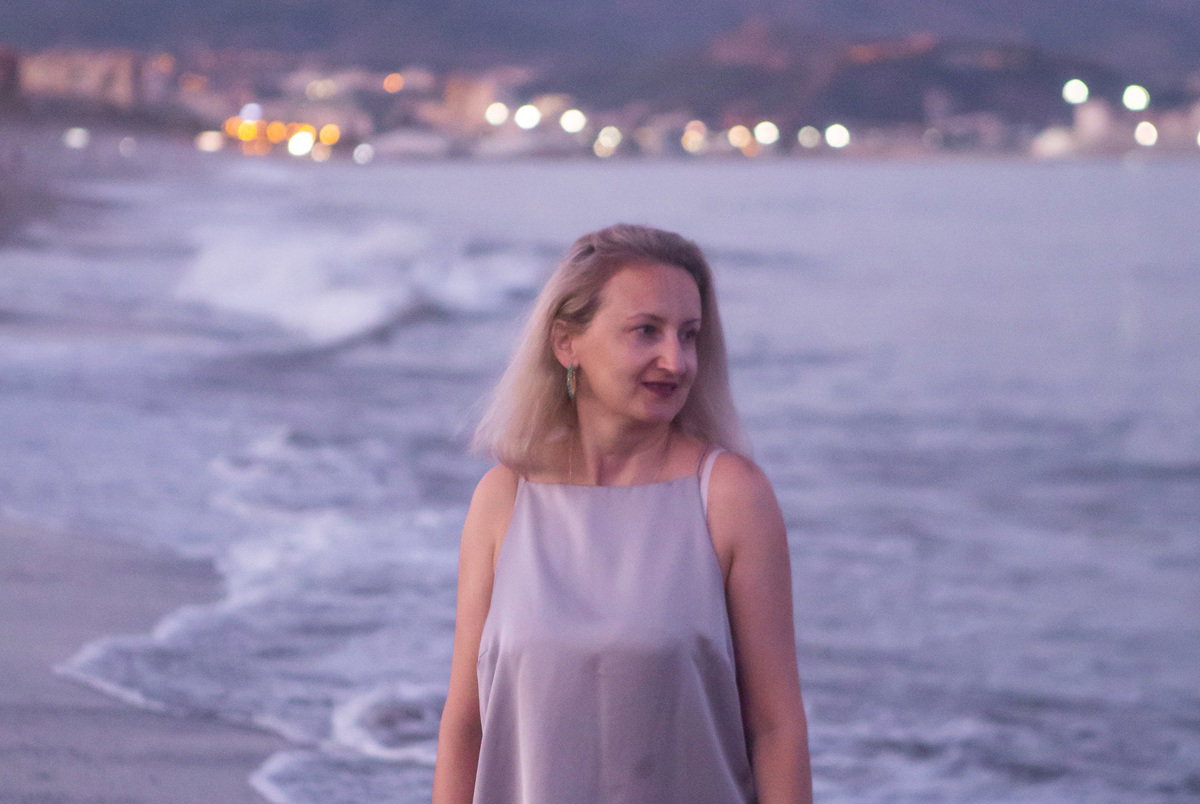 kobieta w wieku 35 plus stoi wieczorem na plaży Costa del Sol w Maladze w Hiszpanii zachwycona