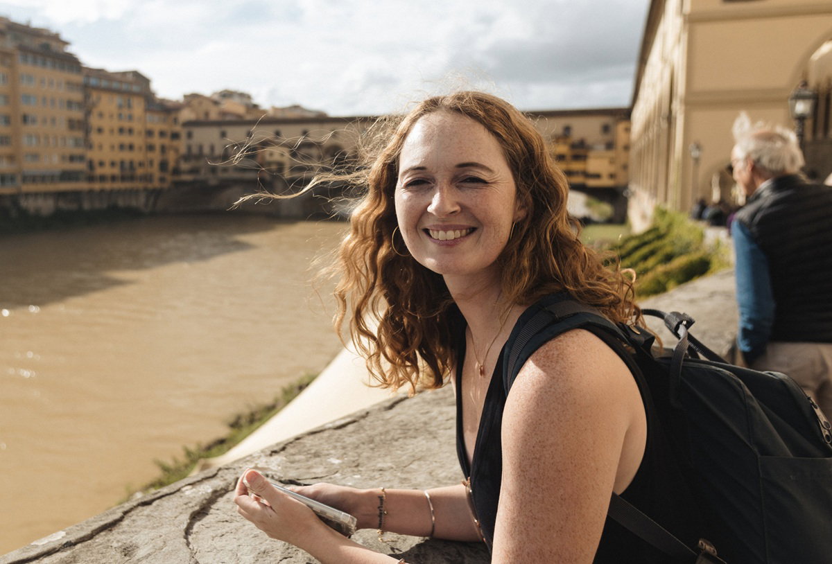 kobieta w wieku 35 plus stoi na mości Ponte Veccio nad rzeką Arno we Florencji i uśmiecha się szeroko