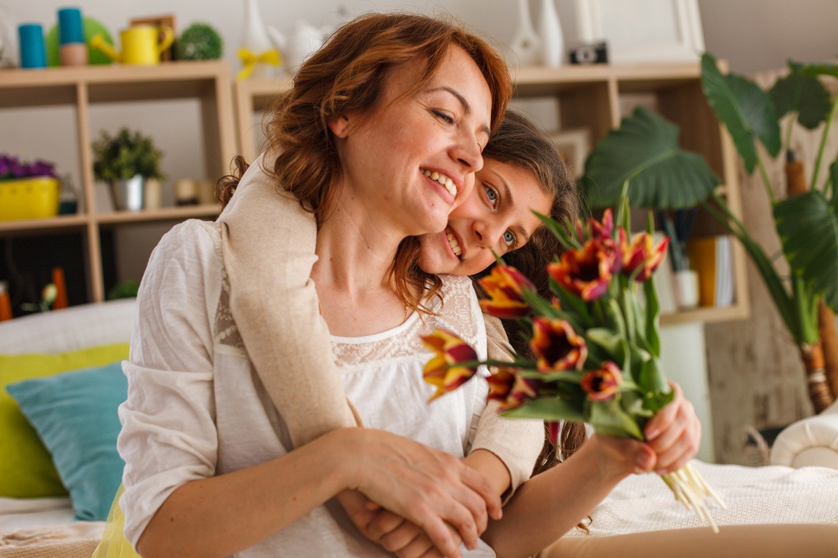 córka w wieku około 9 lat wręcza bukiet tulipanów mamie w wieku 35 plus