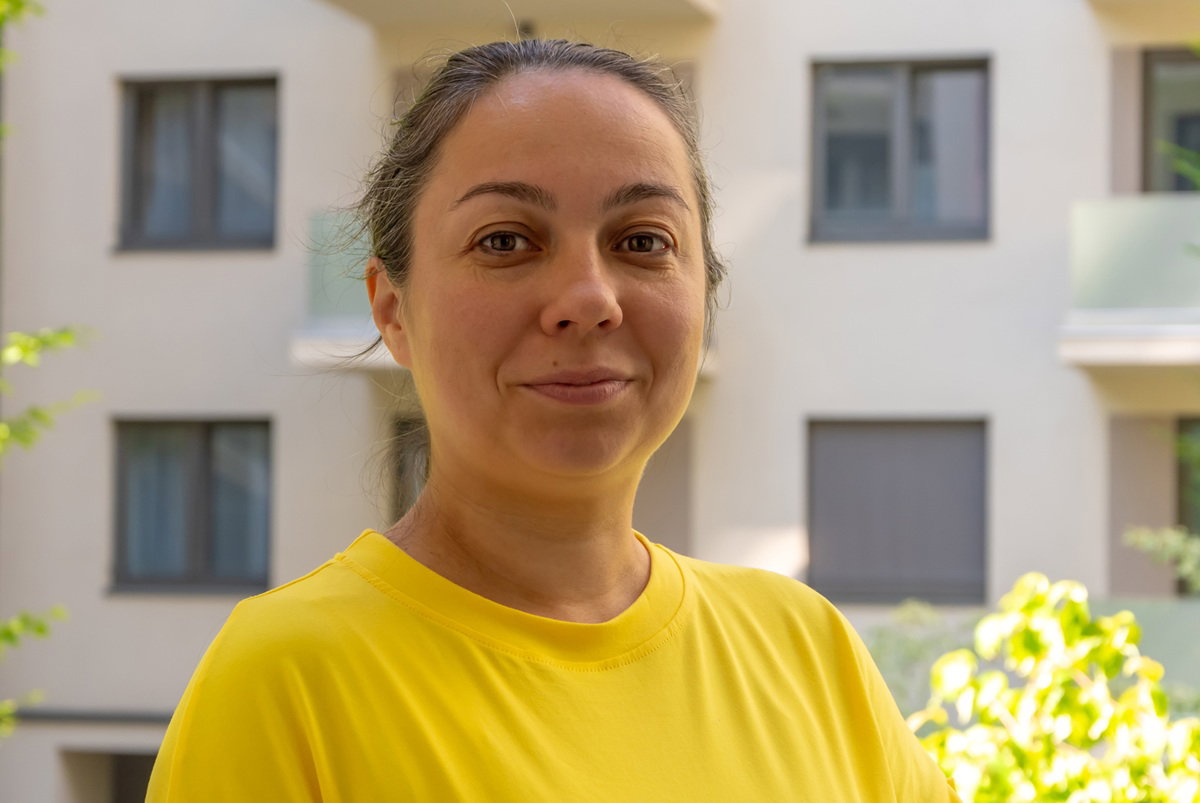 kobieta w wieku 40 plus w żółtej koszulce stoi na balkonie i lekko się uśmiecha