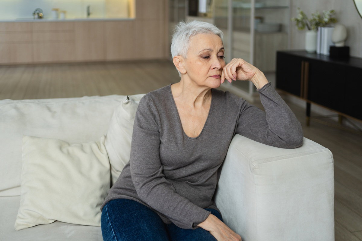 kobieta w wieku 60 plus siwa krótko ostrzyżona siedzi na kanapie zamyślona