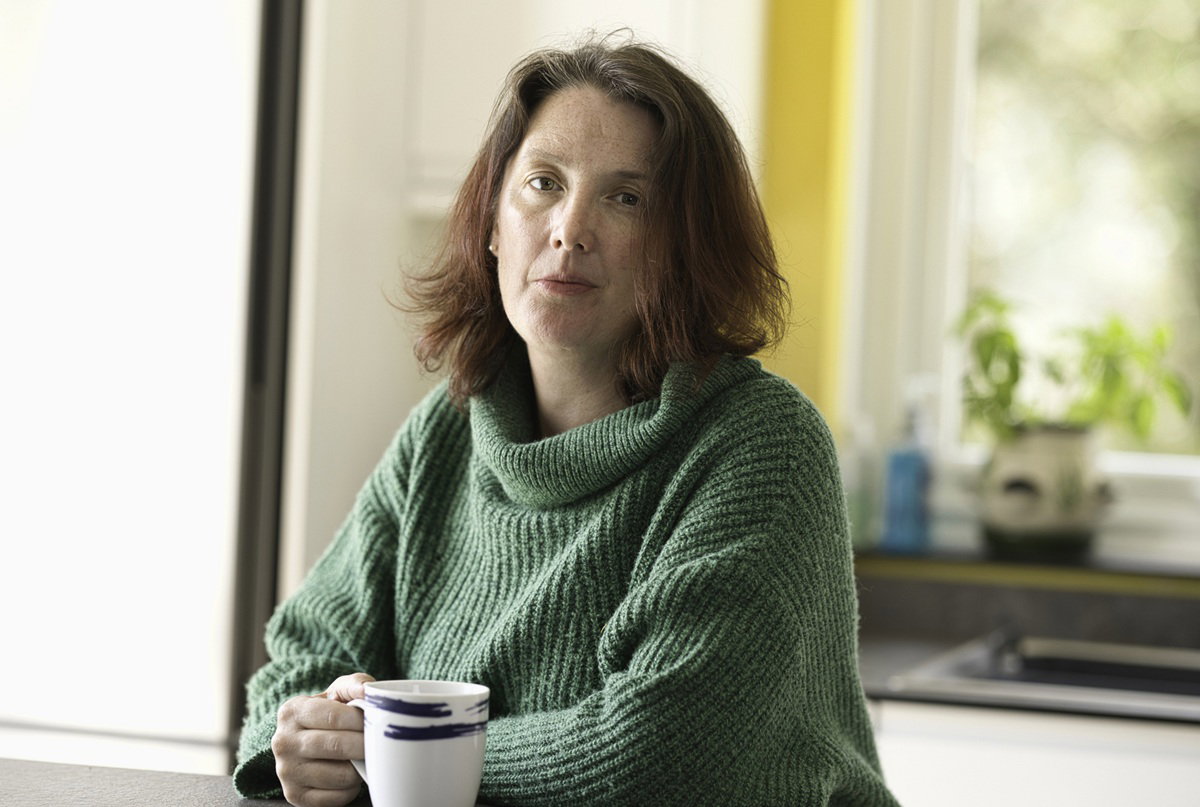 kobieta w wieku 45 plus w zielonym swetrze siedzi w kuchni z kubkiem herbaty smutna