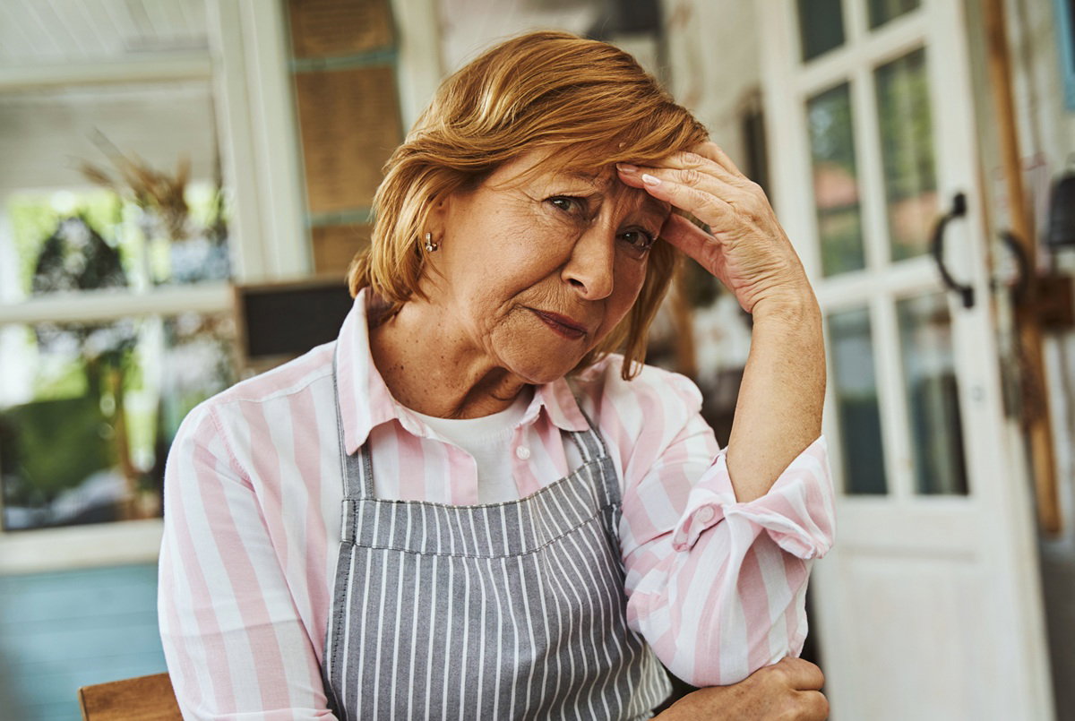 kobieta w wieku 60 plus w fartuszku siedzi zmartwiona na tarasie