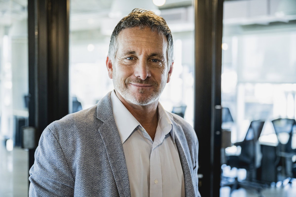 mężczyzna w wieku 40 plus w marynarce stoi na tle biura i lekko się uśmiecha