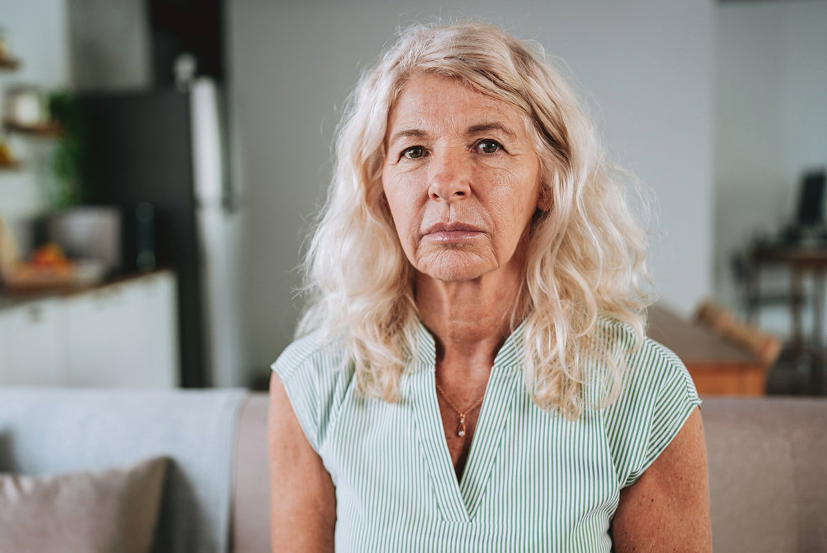 kobieta w wieku 60 plus blondynka siedzi na kanapie z poważną miną