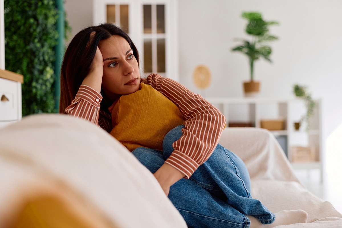 kobieta 30 plus siedzi na kanapie z poduszką w słonecznym salonie zamyślona