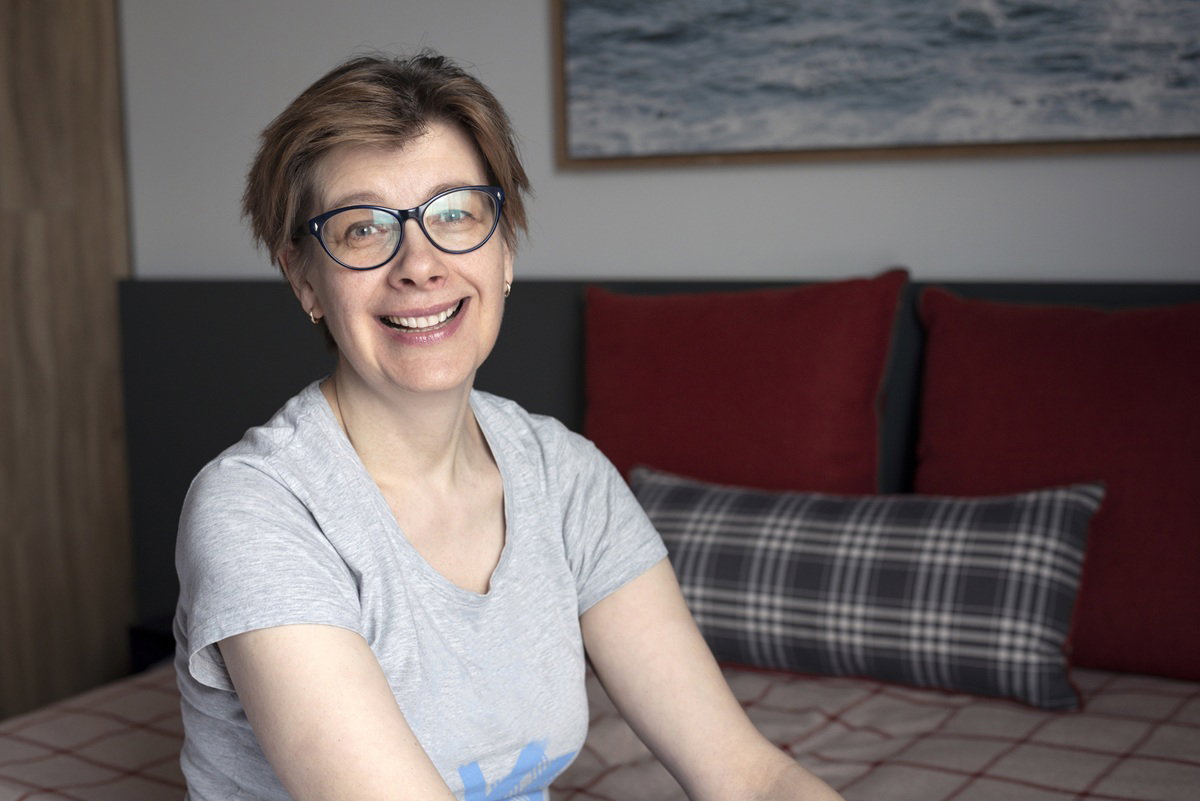 kobieta w wieku 50 plus w okularach siedzi na łóżku i zaśmiewa się przekornie