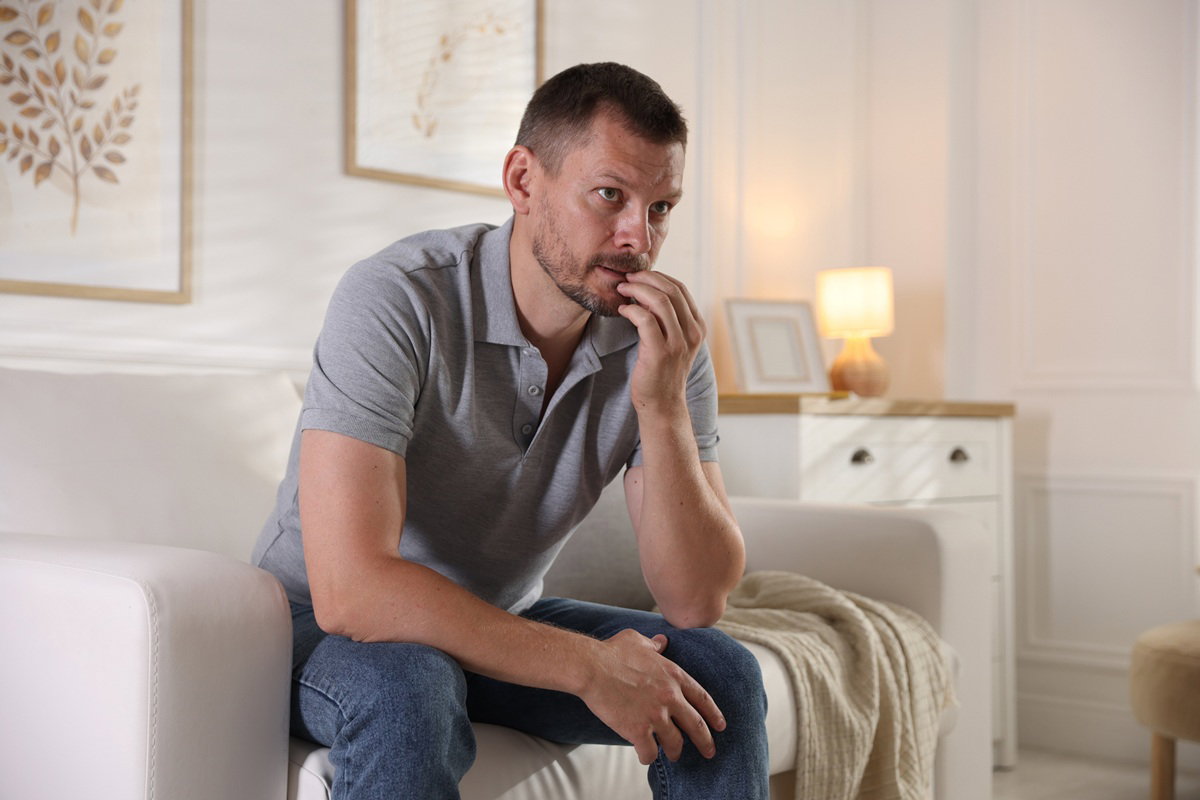 mężczyzna w wieku 40 plus z wąsami i brodą siedzi na kanapie zmartwiony i załamany