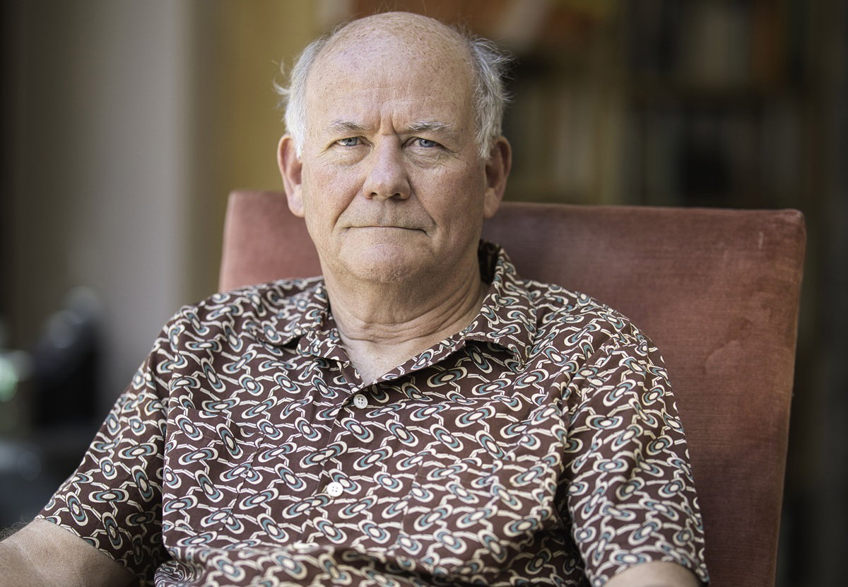mężczyzna w wieku 60 plus we wzorzystej koszuli siedzi w fotelu z poważną miną