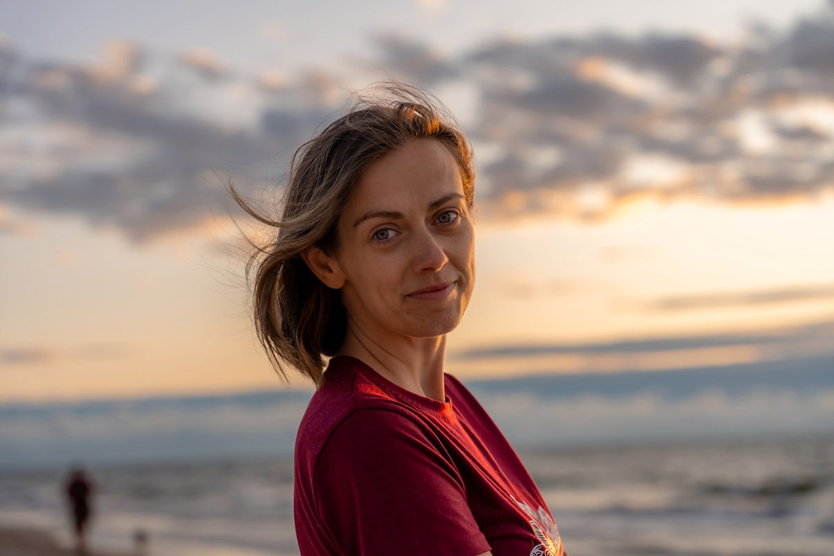 kobieta w wieku 35 plus stoi na tle zachodzącego słońca nad morzem lekko się uśmiecha