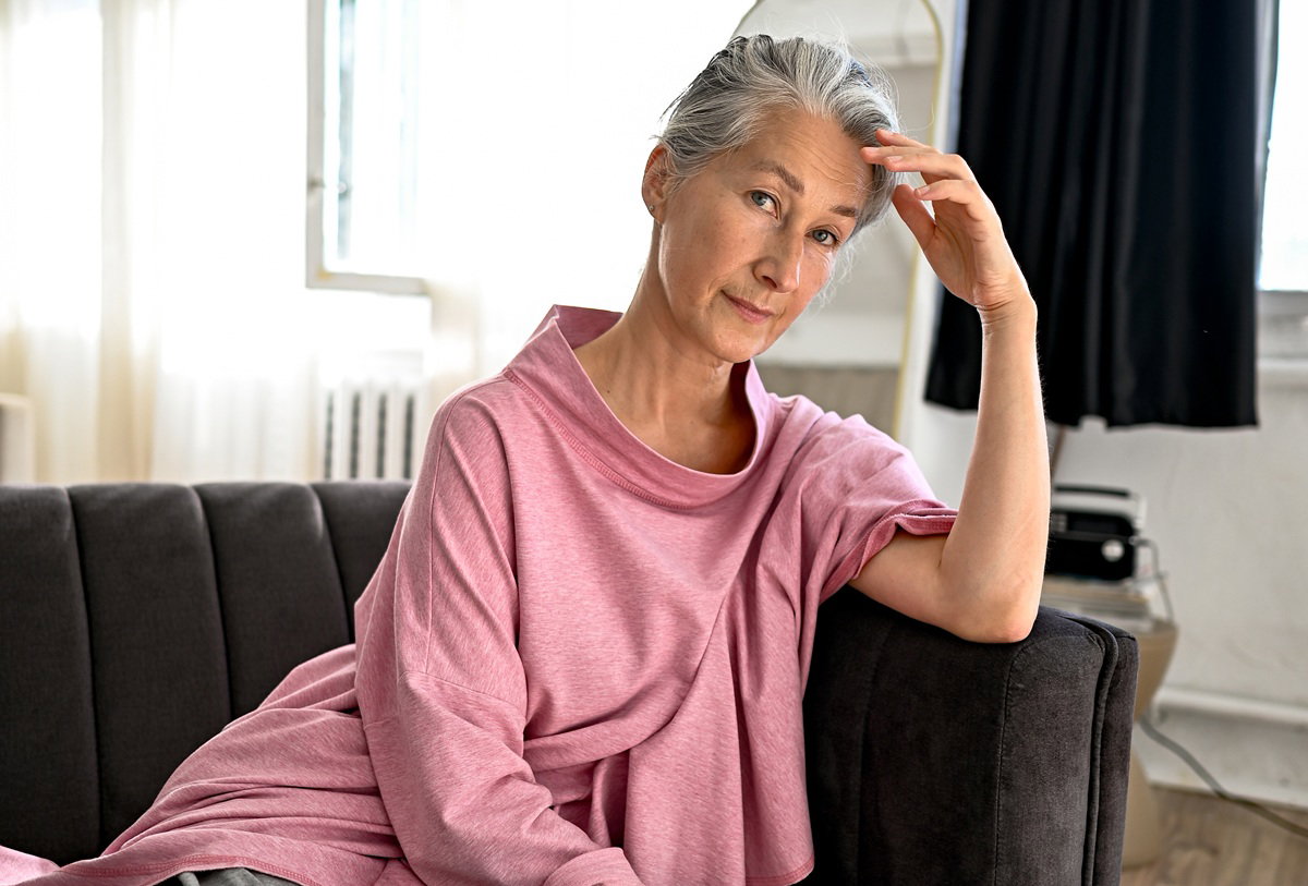 kobieta w wieku 65 plus w różowej bluzce siedzi na sobie z poważną miną