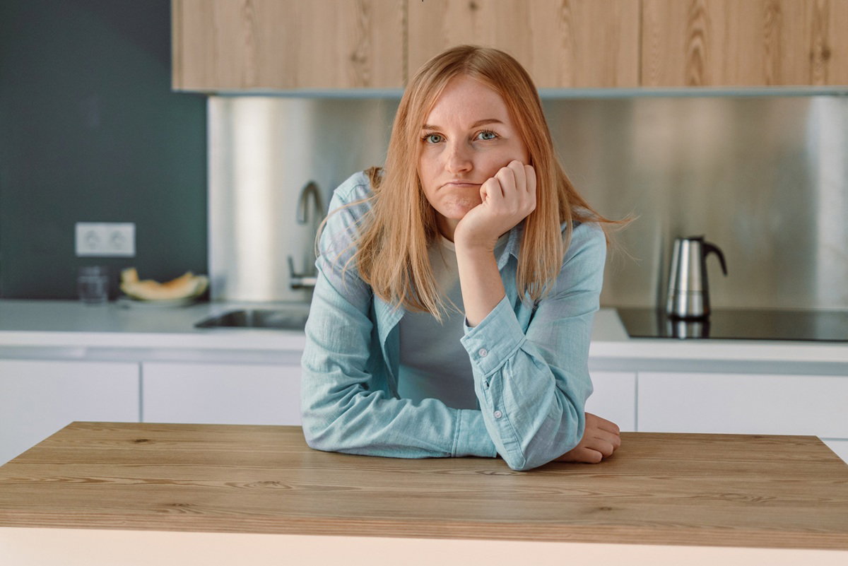 kobieta w wieku 30 plus stoi w pustej kuchni zdegustowana i zmartwiona