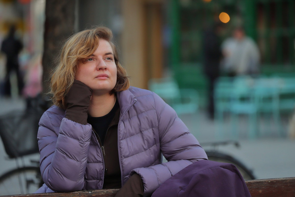 kobieta w wieku 35 plus siedzi na ławce w fioletowej kurtce zamyślona