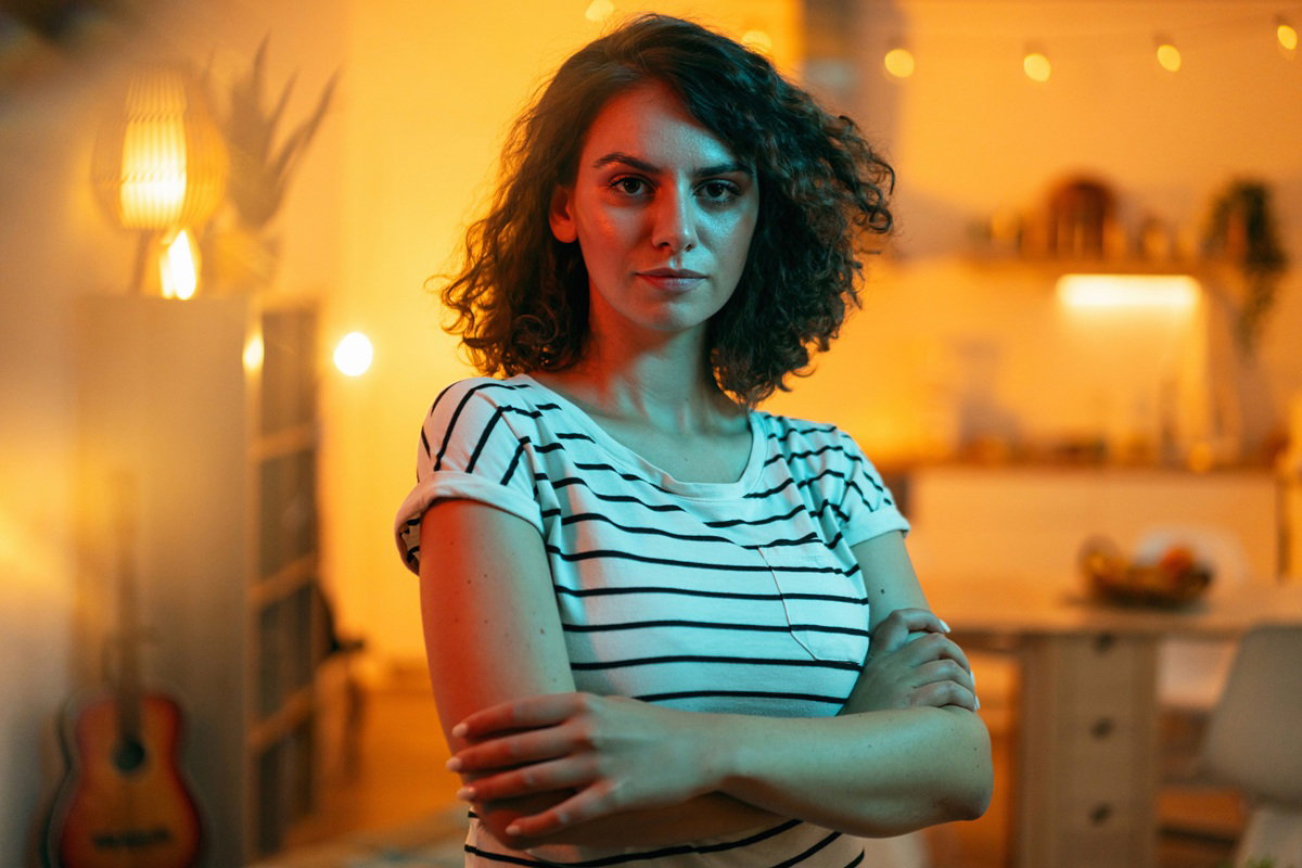 kobieta w wieku 25 plus stoi z poważną miną na tle pokoju wieczorem