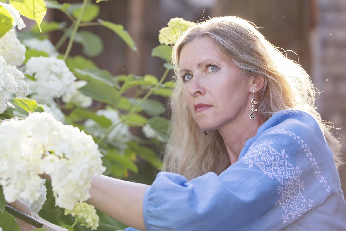 kobieta w wieku 43 plus smutna w niebieskiej bluzce pielęgnuje hortensje w ogrodzie