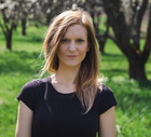 kobieta w wieku 30 plus w czarnej koszulce stoi na tle drzew i patrzy pod słońce