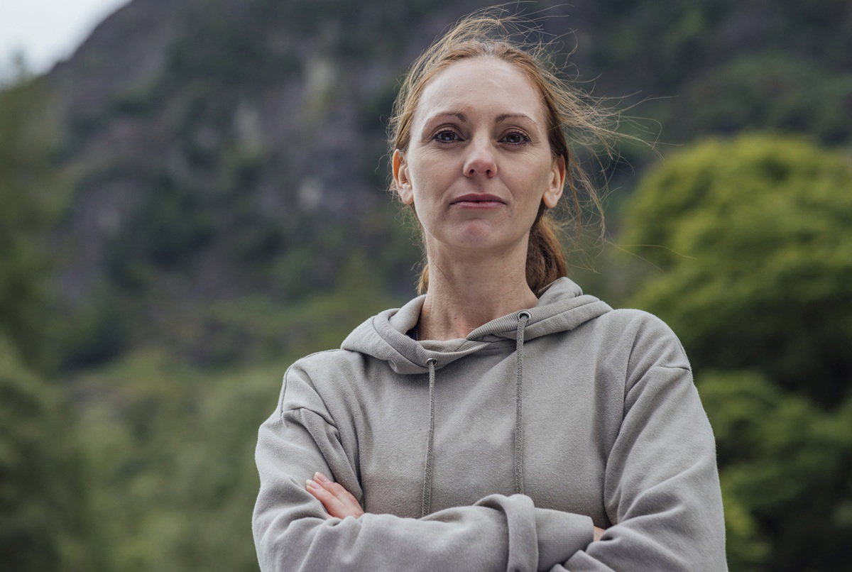 kobieta w wieku 40 plus w szarej bluzie stoi na tle gór zamyślona i smutna