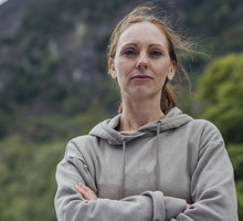 kobieta w wieku 40 plus w szarej bluzie stoi na tle gór zamyślona i smutna