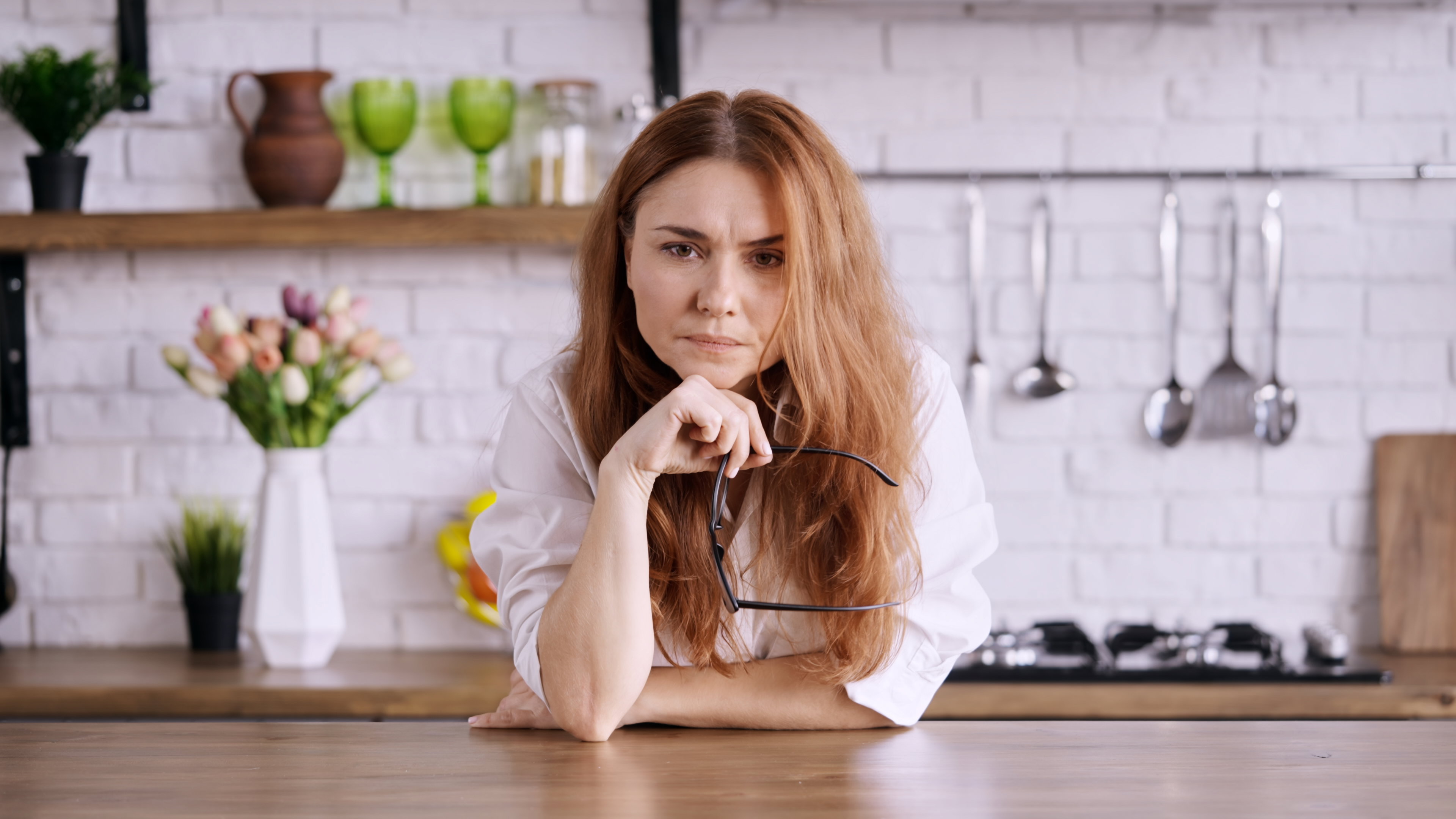 Caucasian female with her glasses in hand worried in a kitchen