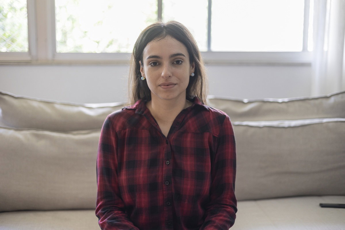 kobieta w wieku 35 plus w kraciastej koszuli siedzi na kanapie na tle okna zamyślona