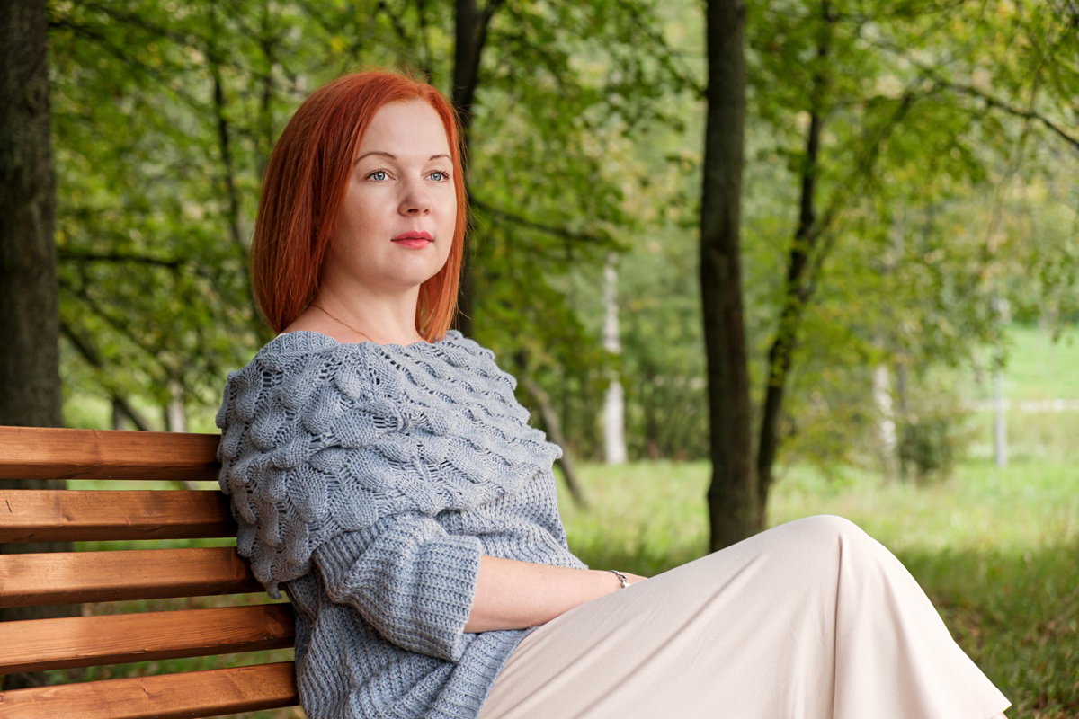 kobieta w wieku 35 plus z marchewkowymi włosami siedzi na ławce w parku zamyślona