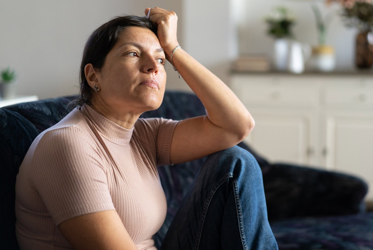 kobieta w wieku 40 plus siedzi na kanapie smutna i zamyślona