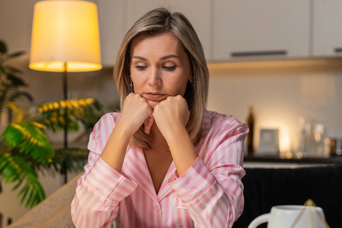 kobieta w wieku 30 plus w pasiastej piżamie siedzi przy stole zmartwiona
