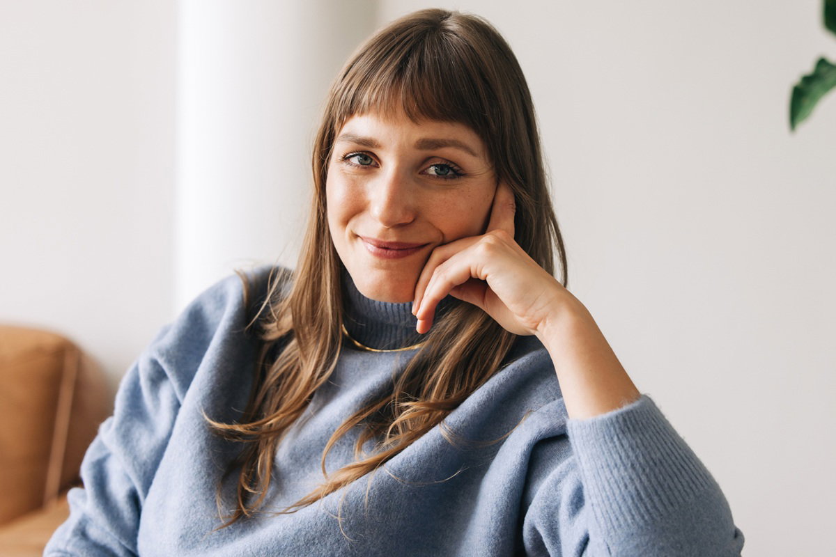 kobieta w wieku 30 plus w niebieskim swetrze siedzi na kanapie z kpiącą miną