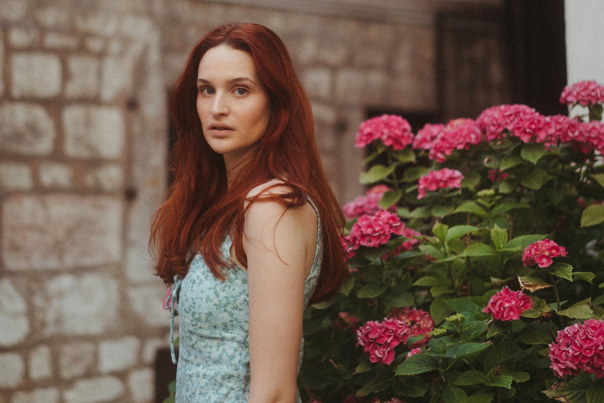 kobieta w wieku 35 plus z długimi rudymi włosami stoi przed domem smutna