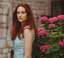 kobieta w wieku 35 plus z długimi rudymi włosami stoi przed domem smutna