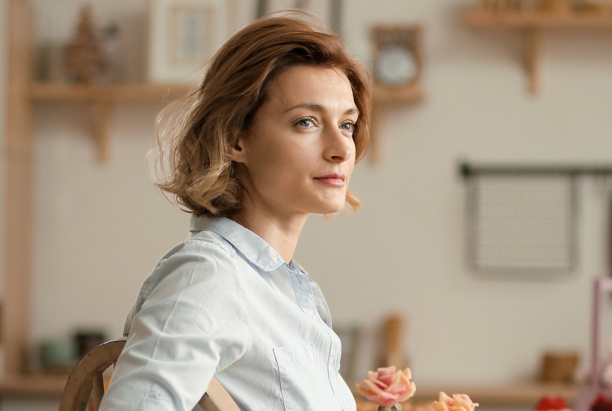 kobieta w wieku 35 plus siedzi przy stole zamyślona i smutna z kwiatami w ręce