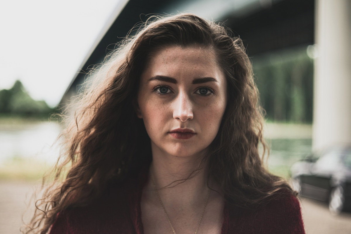 kobieta w wieku 25 plus z długimi pofalowanymi włosami stoi na zewnątrz poważna