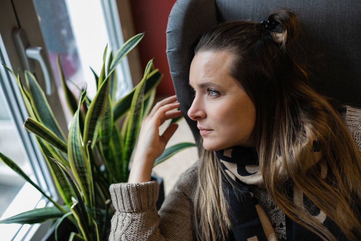 kobieta w wieku 30 plus siedzi na fotelu i patrzy zamyślona w okno