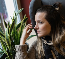 kobieta w wieku 30 plus siedzi na fotelu i patrzy zamyślona w okno