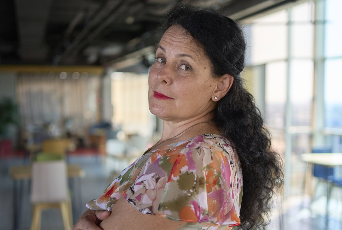 kobieta w wieku 55 plus w kwiecistej sukience z ciemnymi włosami stoi na tle restauracji