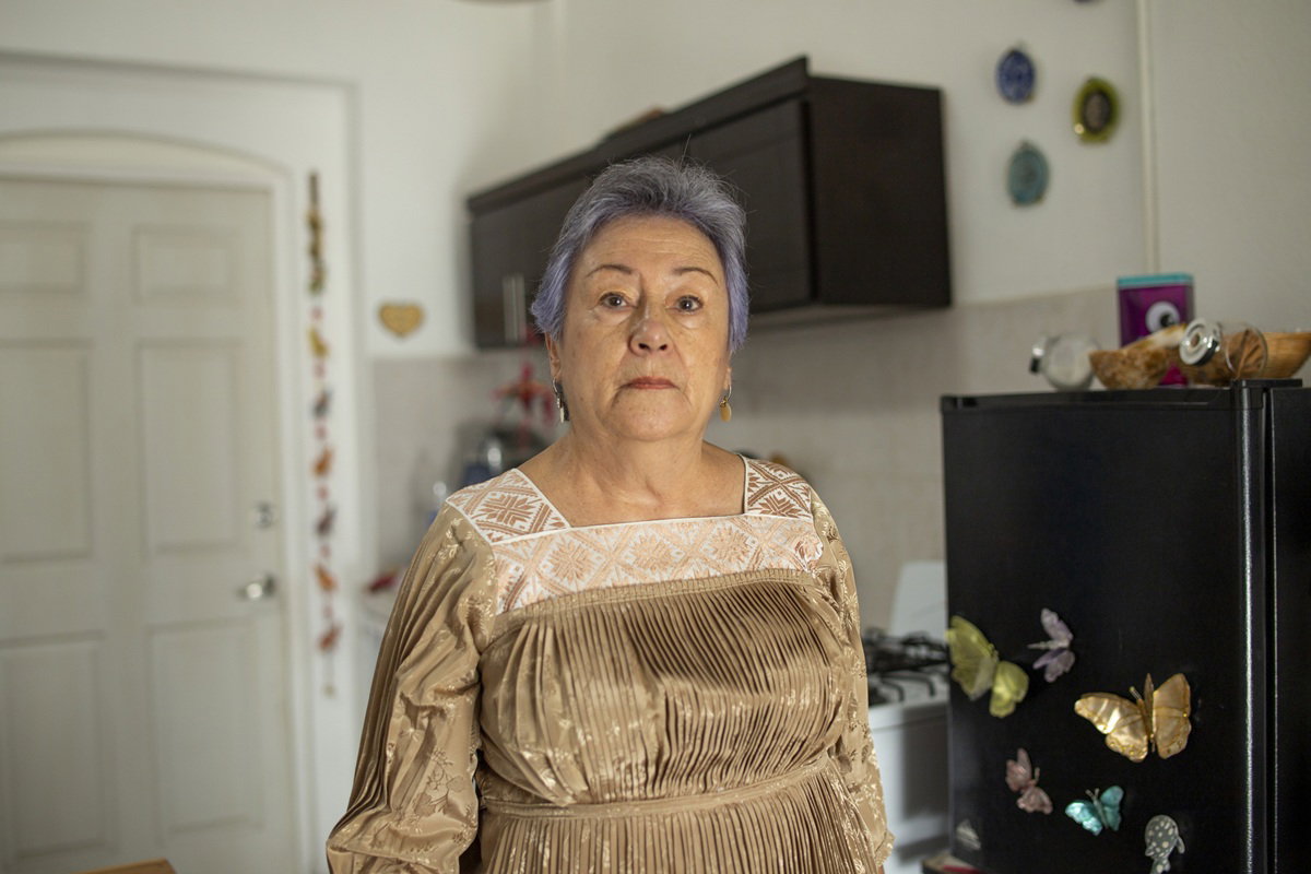 kobieta w wieku 70 plus z fioletowymi włosami stoi w sukience na tle kuchni z poważną miną