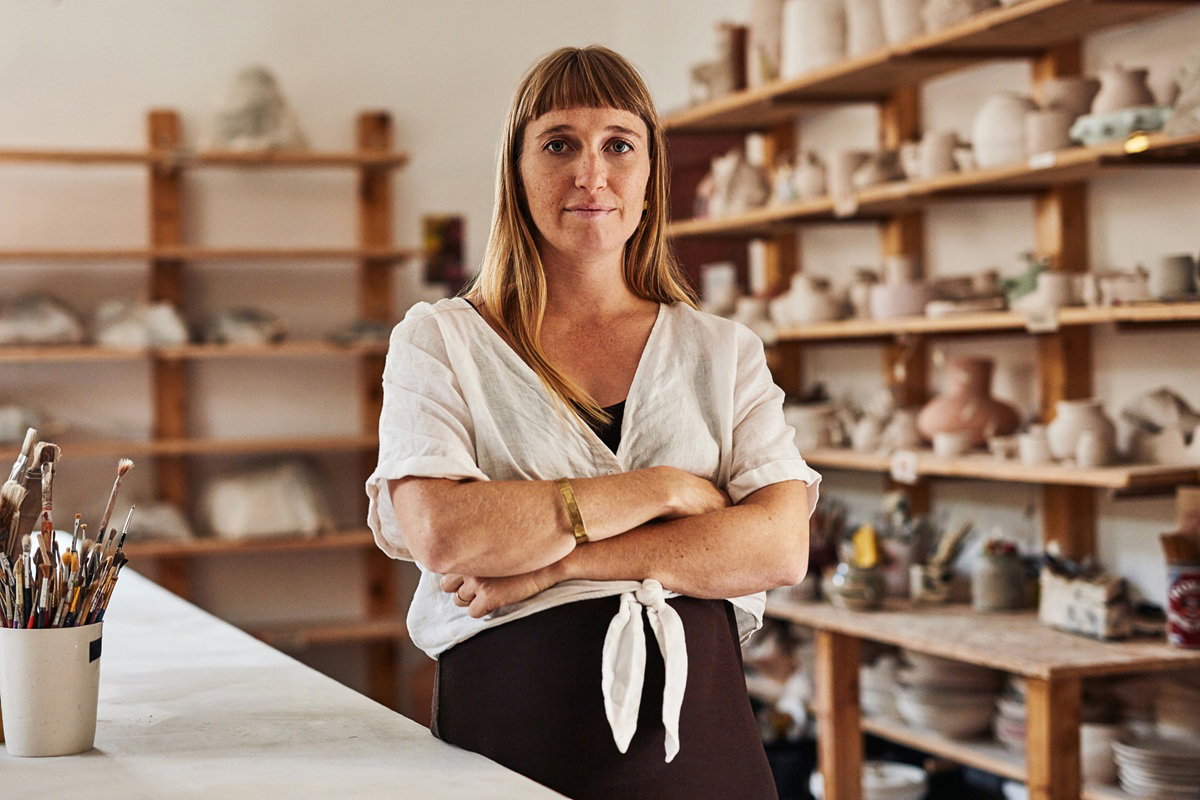 kobieta w wieku 30 plus z piegami stoi w pracowni ceramicznej ze smutną miną