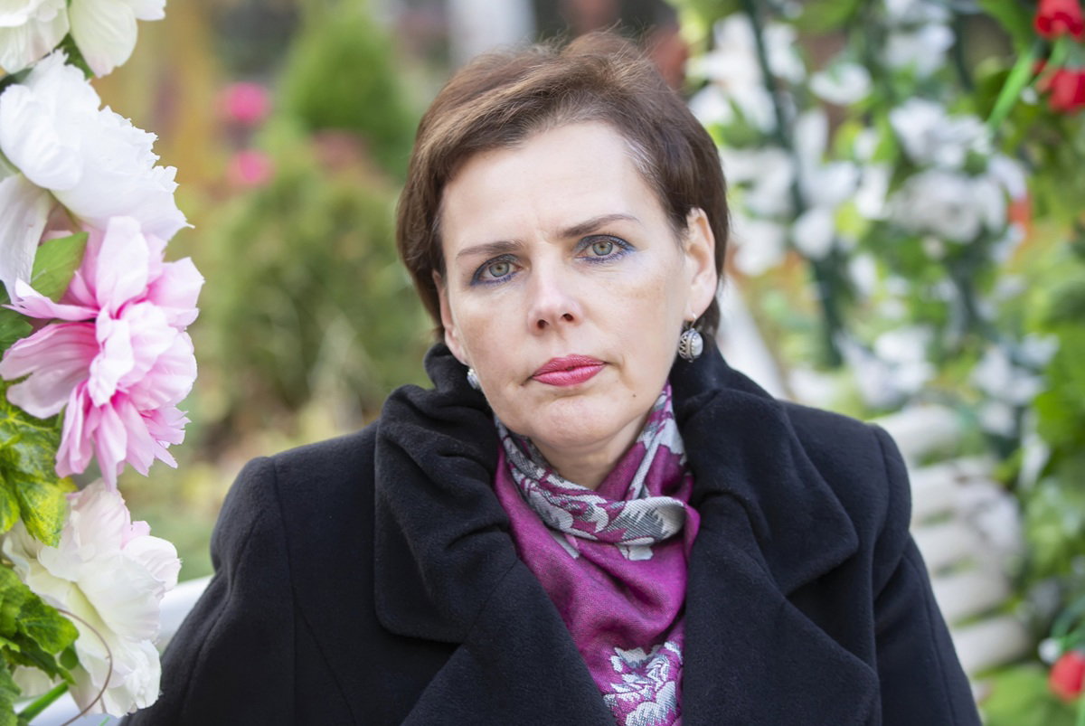 kobieta w wieku 50 plus siedzi na tle kwiecistych dekoracji ze zmartwioną miną