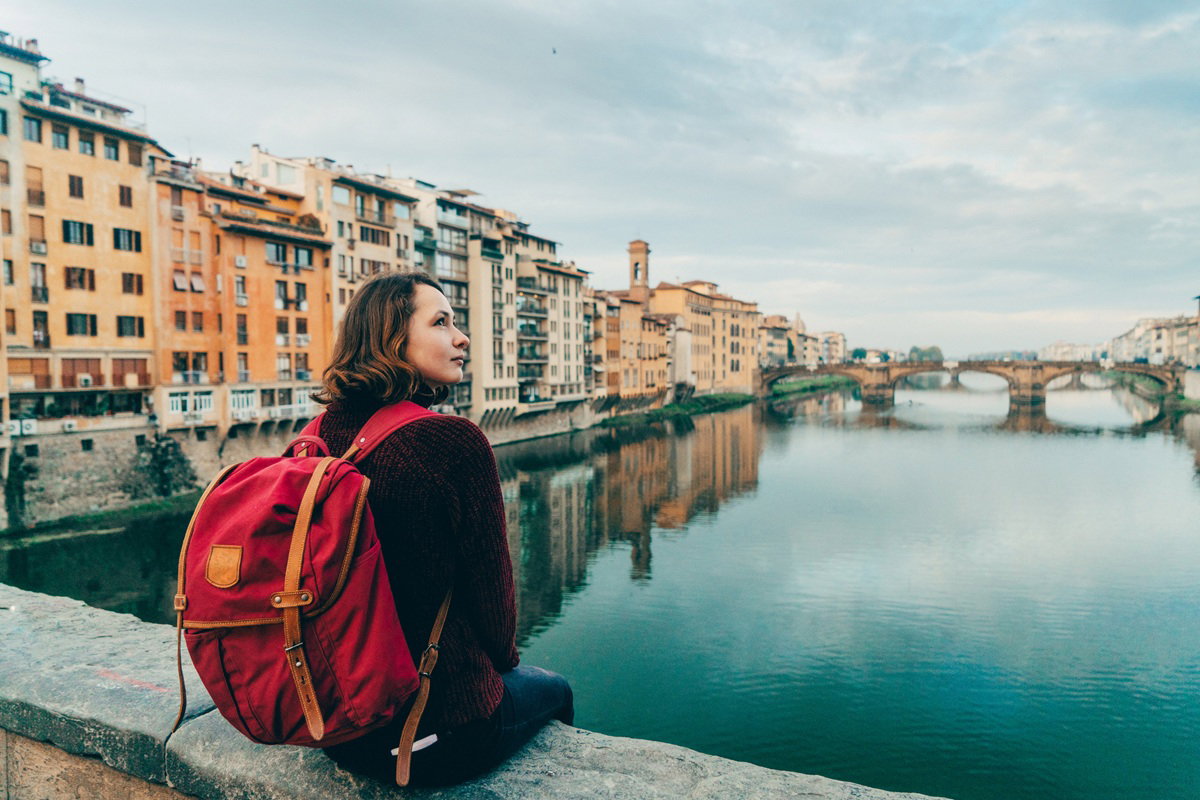 kobieta w wieku 35 plus siedzi na Ponte Vecchio we Florencji nad rzeką Arno z plecakiem zamyślona