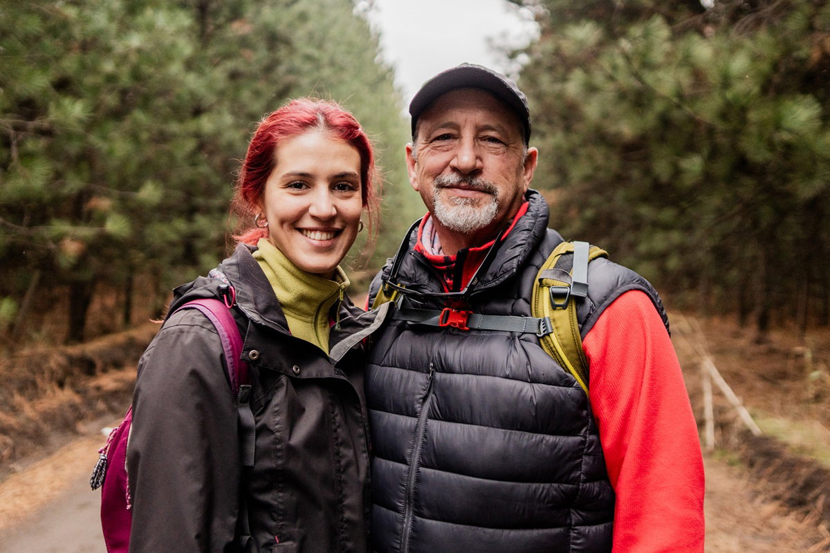 kobieta w wieku 30 plus z mężczyzną w wieku 60 plus stoją na tle lasu uśmiechnięci