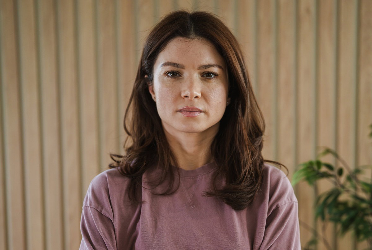 kobieta w wieku 35 plus stoi na tle drewnianej ściany z poważną miną