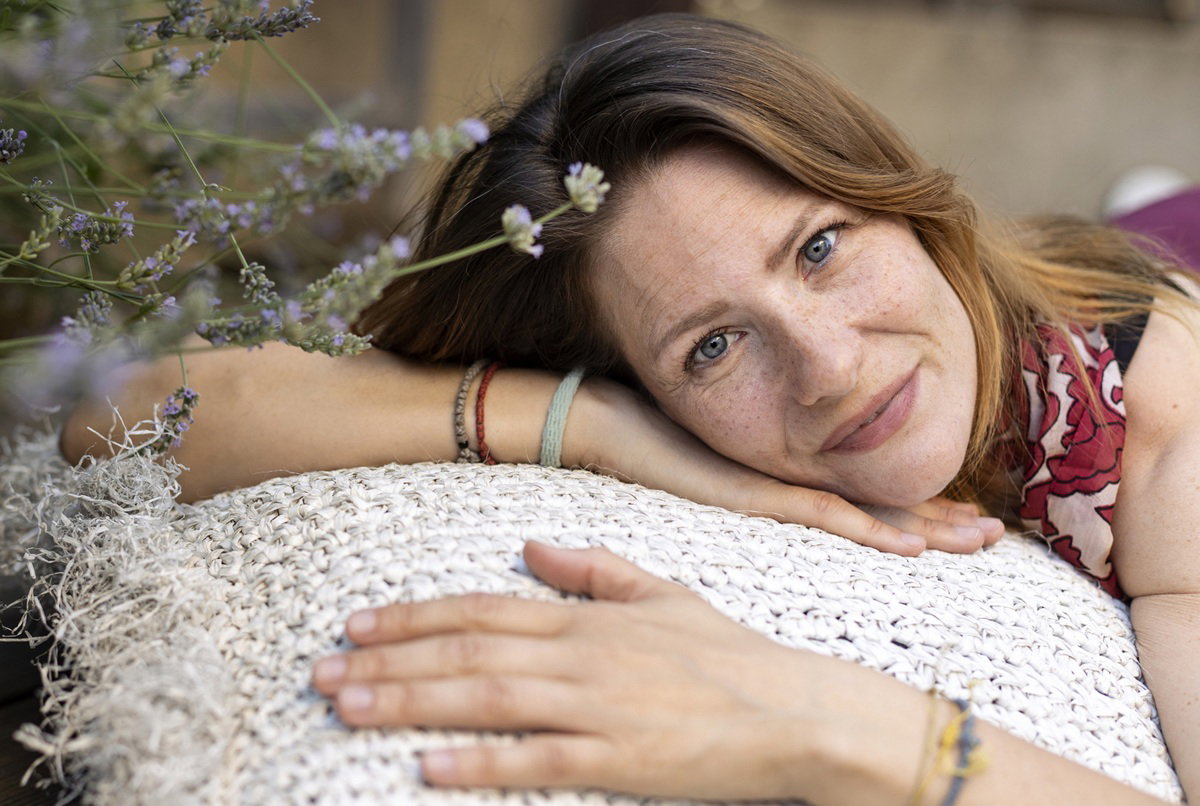 kobieta w wieku 40 plus leży na poduszce na balkonie koło lawendy i lekko się uśmiecha
